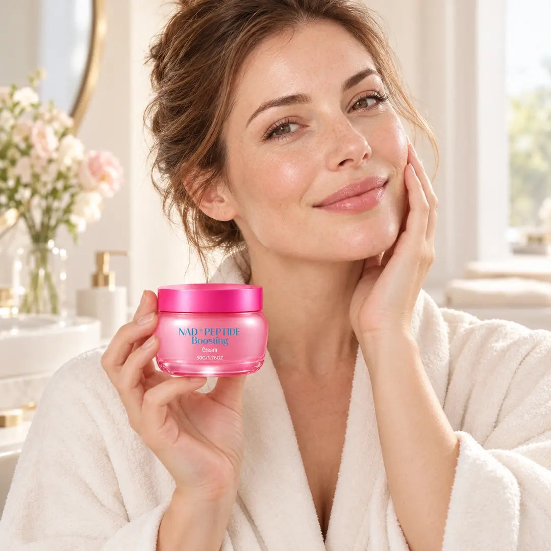 Woman in an ivory robe holding a pink 50 g jar of NAD+ Peptide Boosting Face Cream while gently touching her cheek.