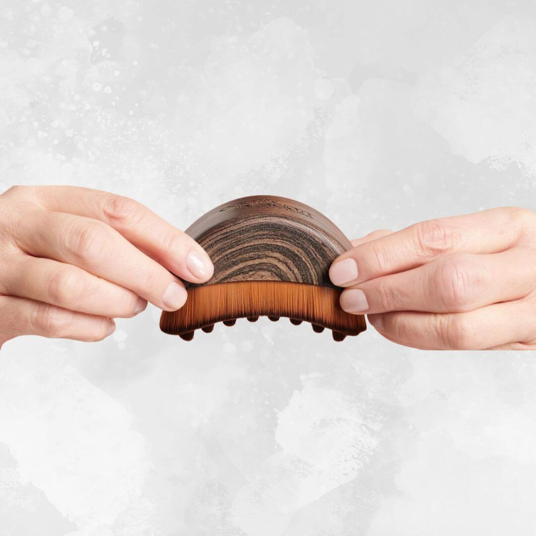 Hands holding a wooden facial lymphatic drainage brush for detox and glowing skin.