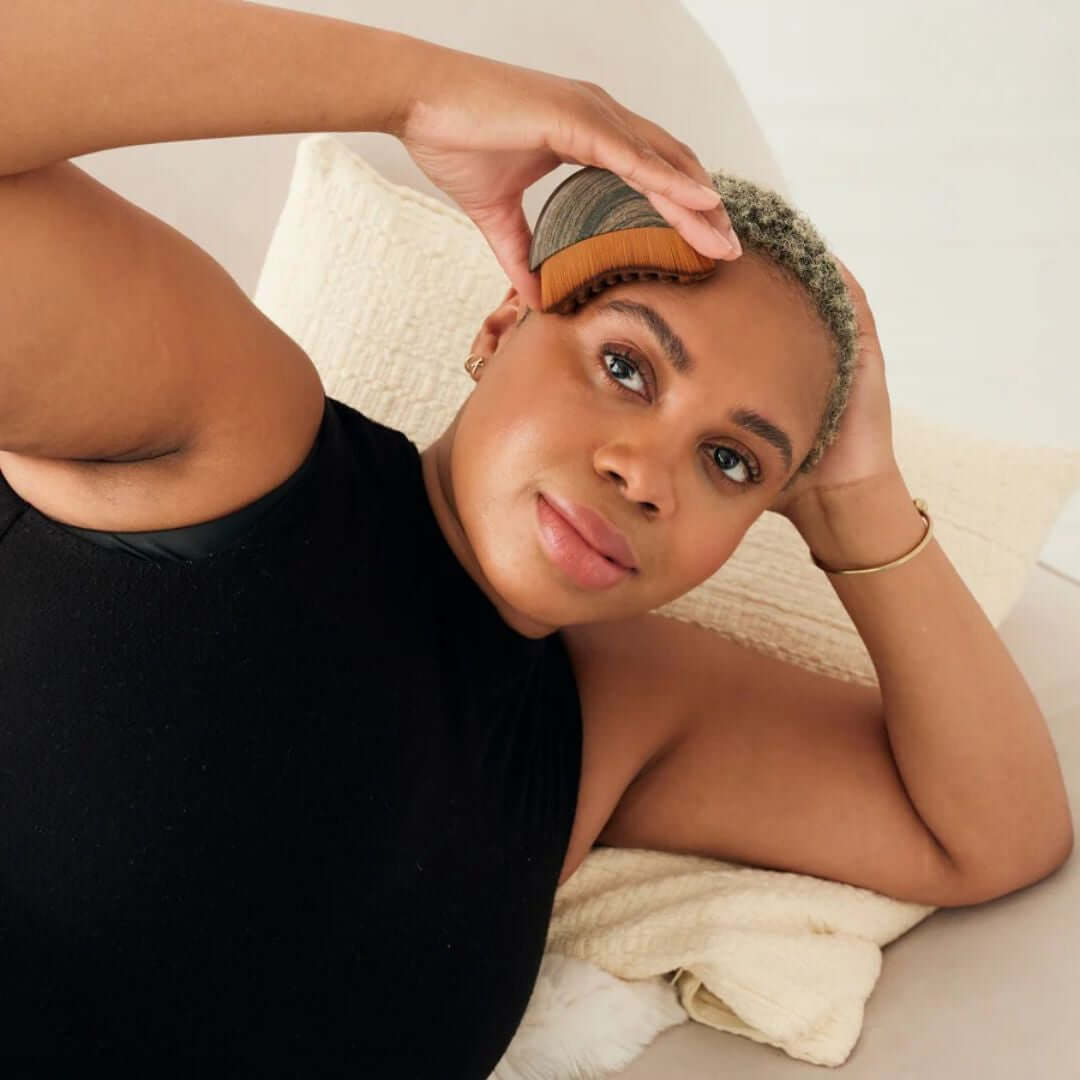 Person using a facial lymphatic drainage brush for detox and glowing skin while relaxing on a couch.